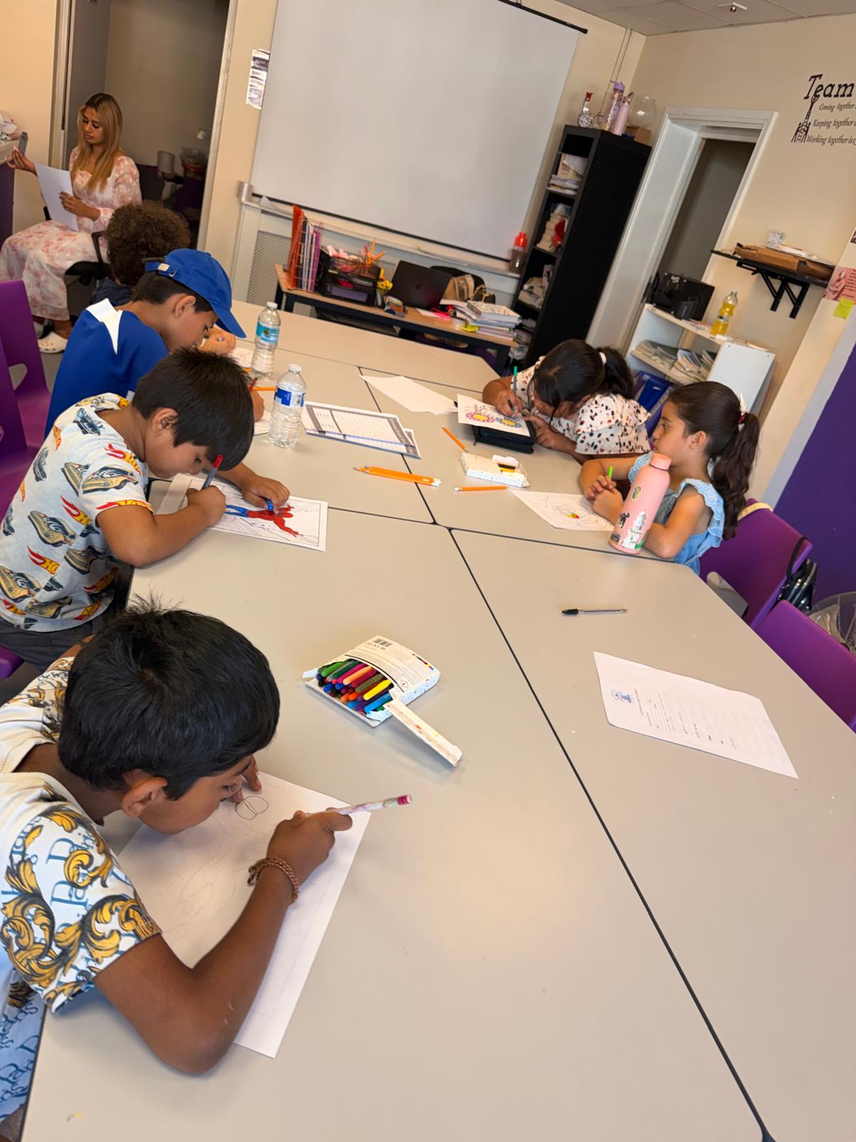 Children seated around a table colouring and completing word activities at the start of the session