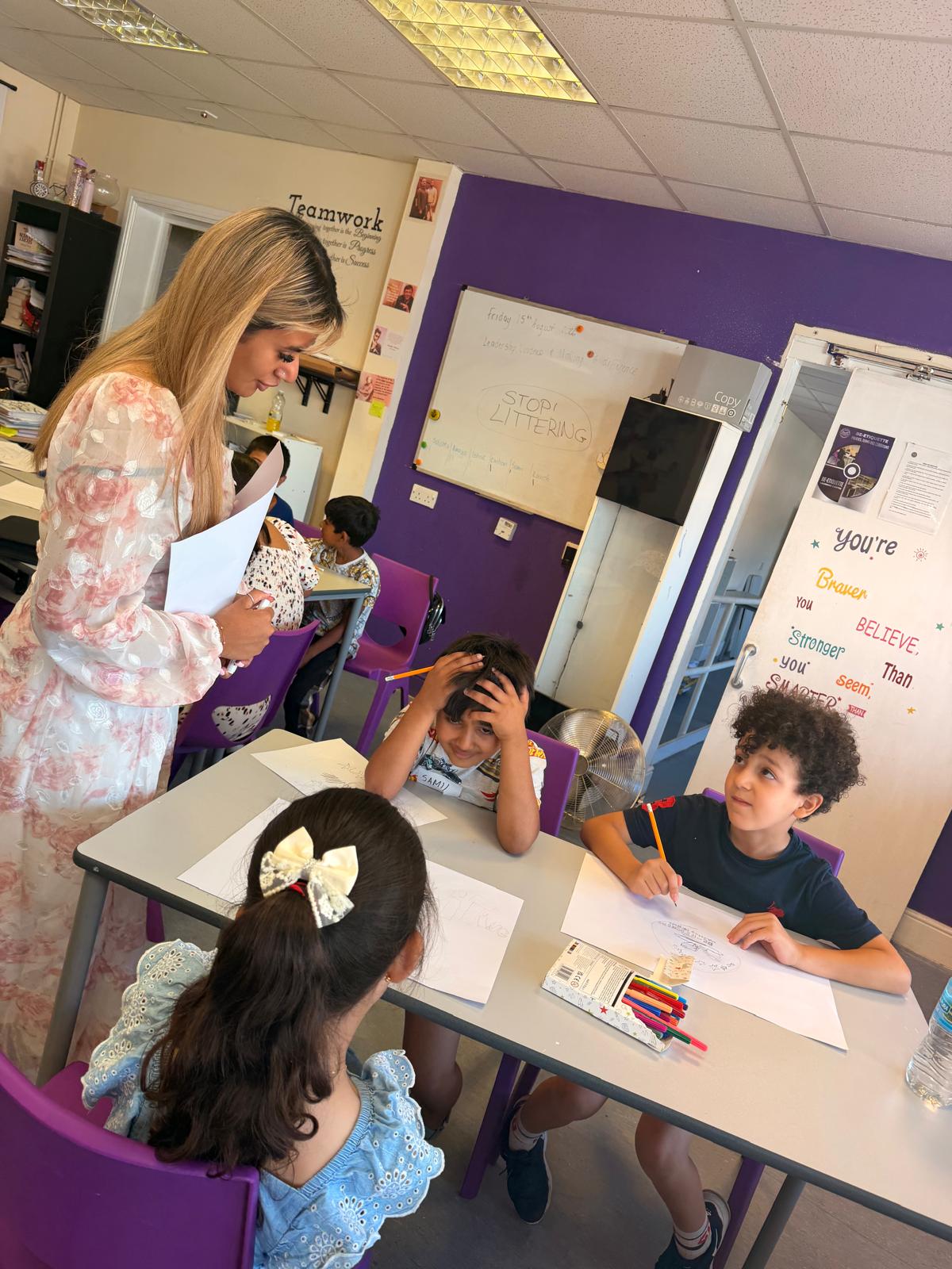 A facilitator talking with children at a table, with a whiteboard behind showing a Stop Littering message