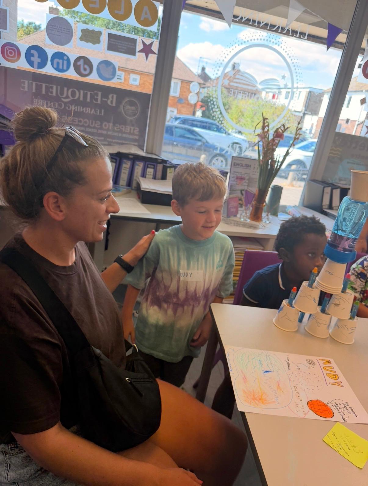 A parent sitting with children beside their drawing and cup-building activity