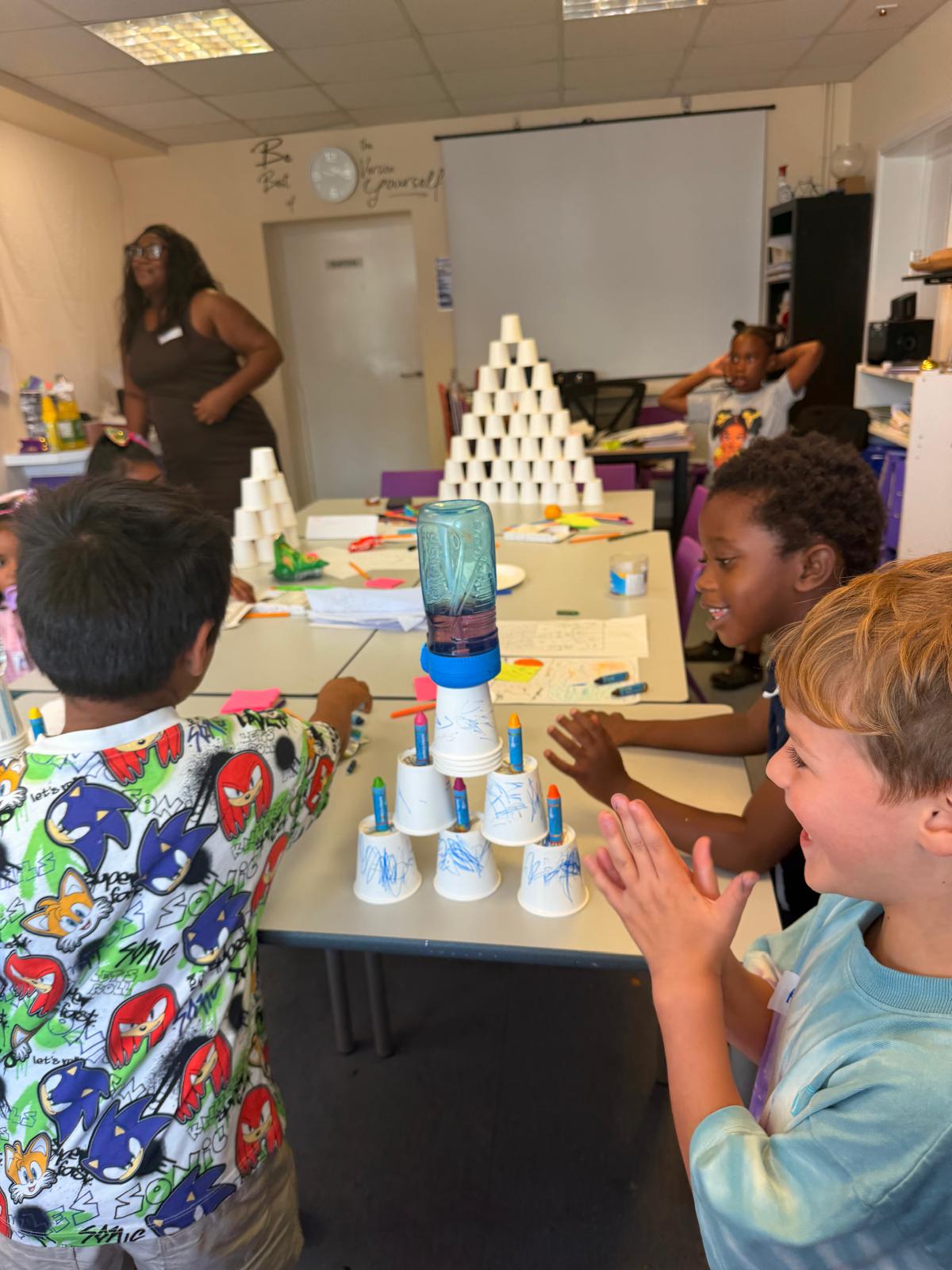 Children working together and clapping as they build a tower of paper cups at a table