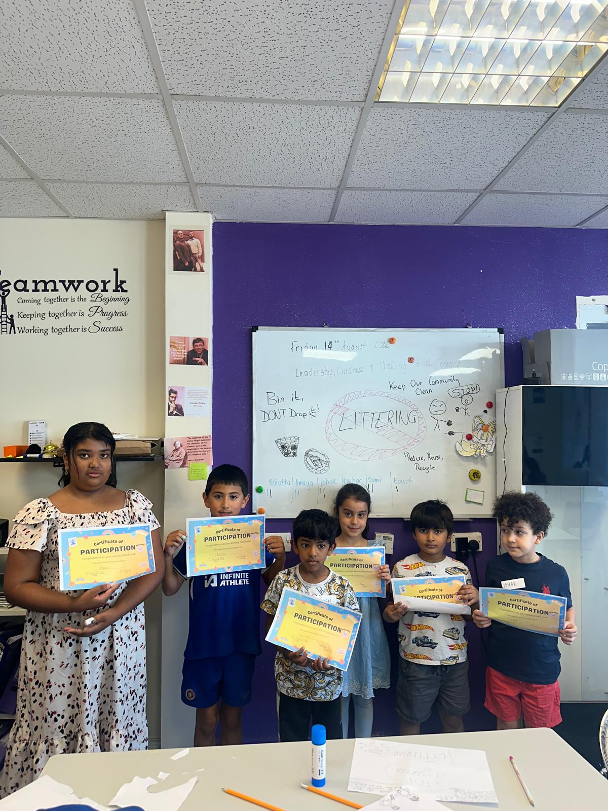 A group of children holding participation certificates in front of a whiteboard with a littering poster